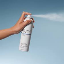 A hand spraying OLAPLEX Nº4D Dry Shampoo into the air against a blue sky background. Featured in the DCHAN SALON blog post