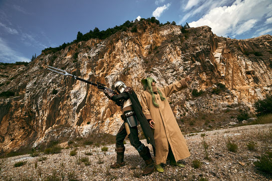 Cosplay Mandaloriano e Grogu Star Wars con collina su sfondo, con arma da fuoco