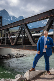Groom posing against canmore train bridge