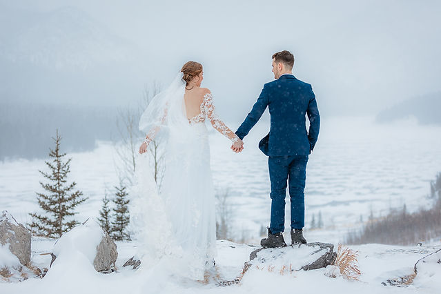 Bride and groom standing on snow covered mountain top