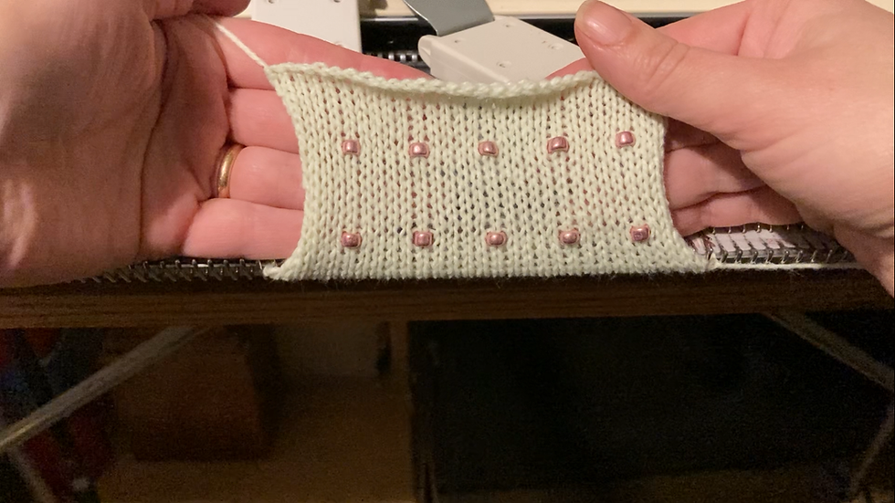 Eye-level view of flat bed knitting machine with partially knitted fabric showing knit and purl stitches