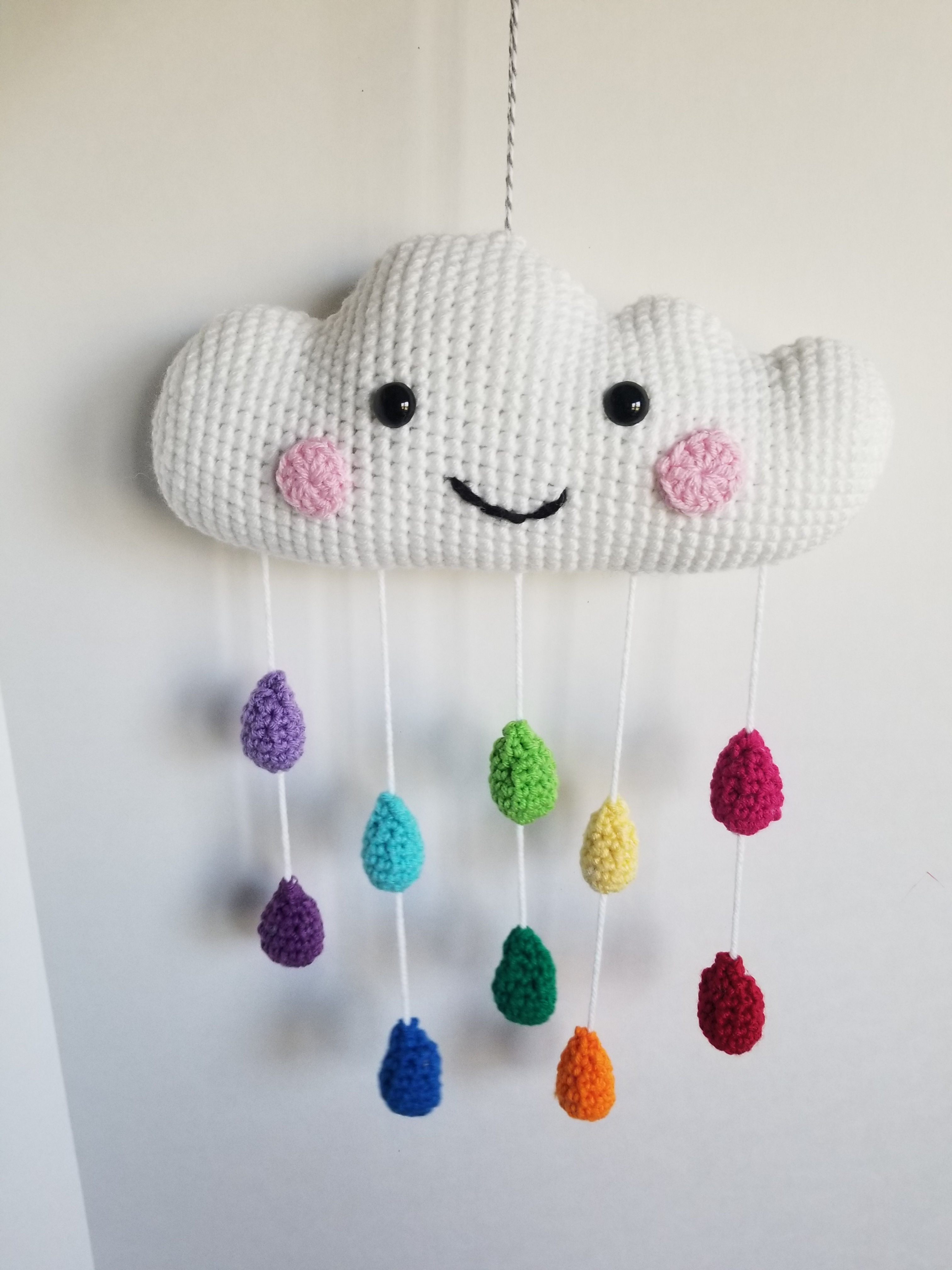 Smiling face on a crochet cloud mobile with a rainbow of crochet rain drops hanging below
