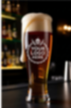 Filled pilsner beer glass mockup on a bar counter, with a large dripping foam head and a placeholder logo.