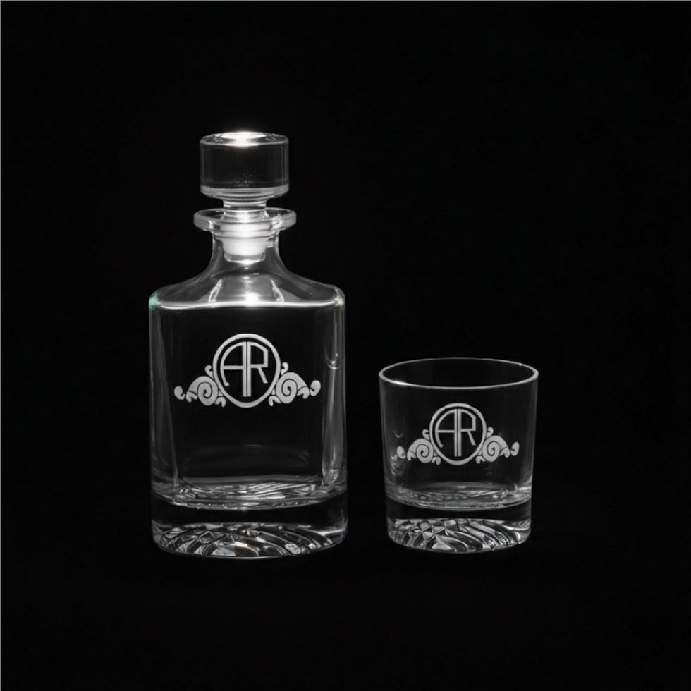 A personalized clear glass whiskey decanter and matching rocks glass, both custom engraved with the monogram initials 'AR' and decorative flourishes, set against a black background.