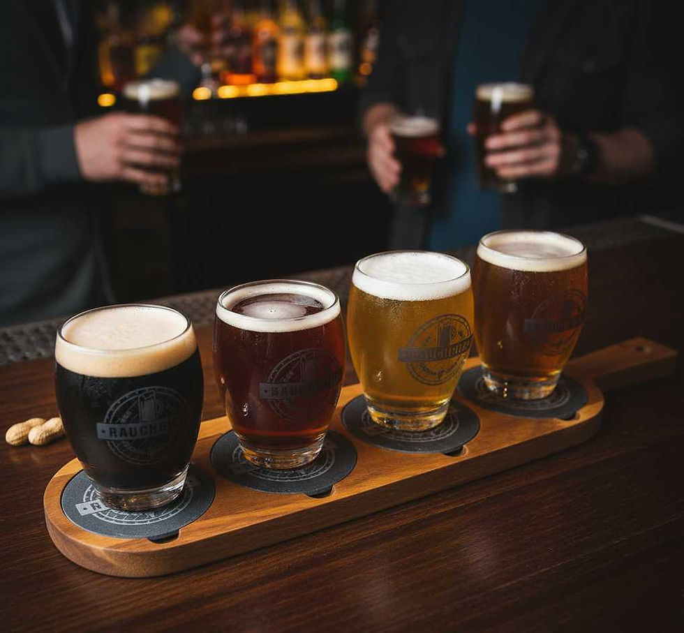 Acacia wood flight board with four craft beers on a dark bar top.