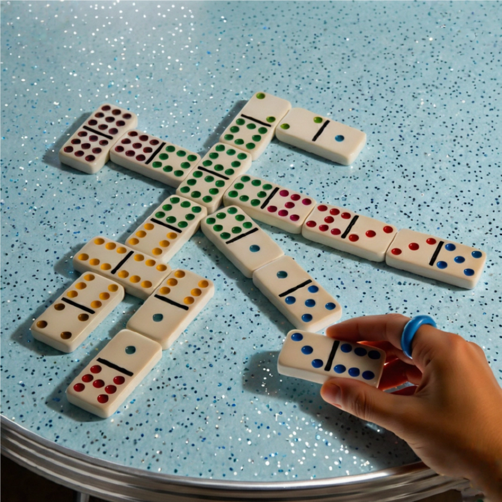 Hand playing dominoes with colored dots on vintage light blue sparkly Formica table.