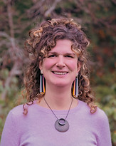 A golden arched window showing Keltie. Keltie is a white woman wearing a purple top, a circular necklace, dangling earrings, and light brown curly hair half up. Keltie is smiling and there are tress in the background.