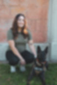 Smiling woman kneels beside dog with "MOLD DOG" vest on grass.