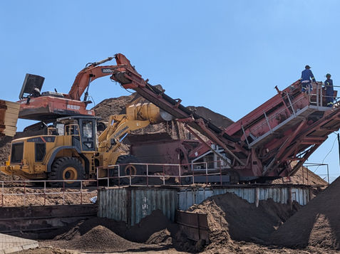 Heavy machinery processing materials on a construction site under a clear sky. Reef Investimentos, Lda