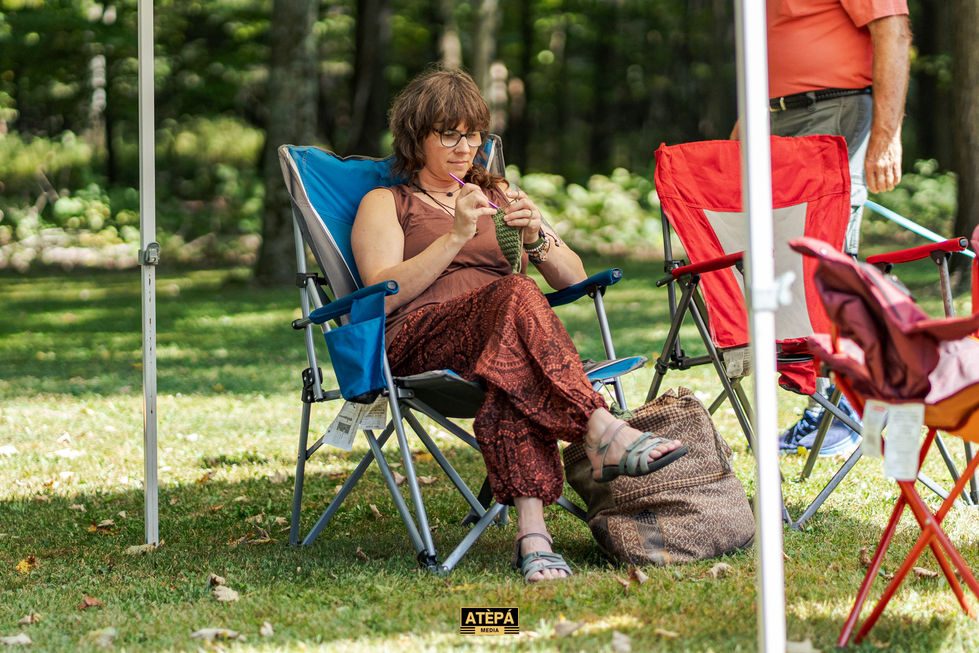 a woman sits in a blue folding chair knitting