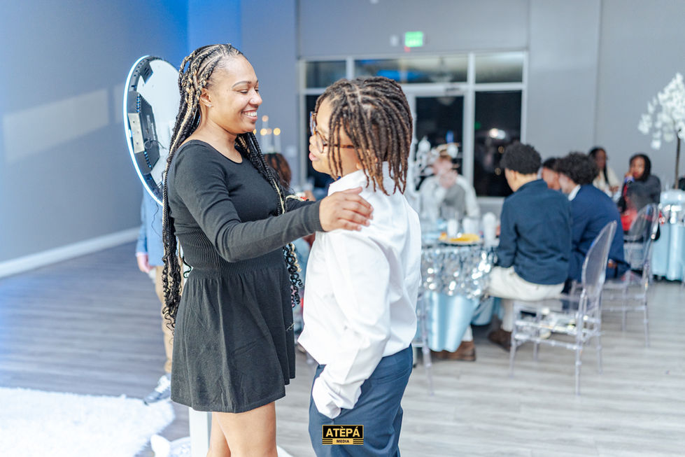 a woman in a black dress is hugging a boy in a white shirt with a tepa logo on the bottom