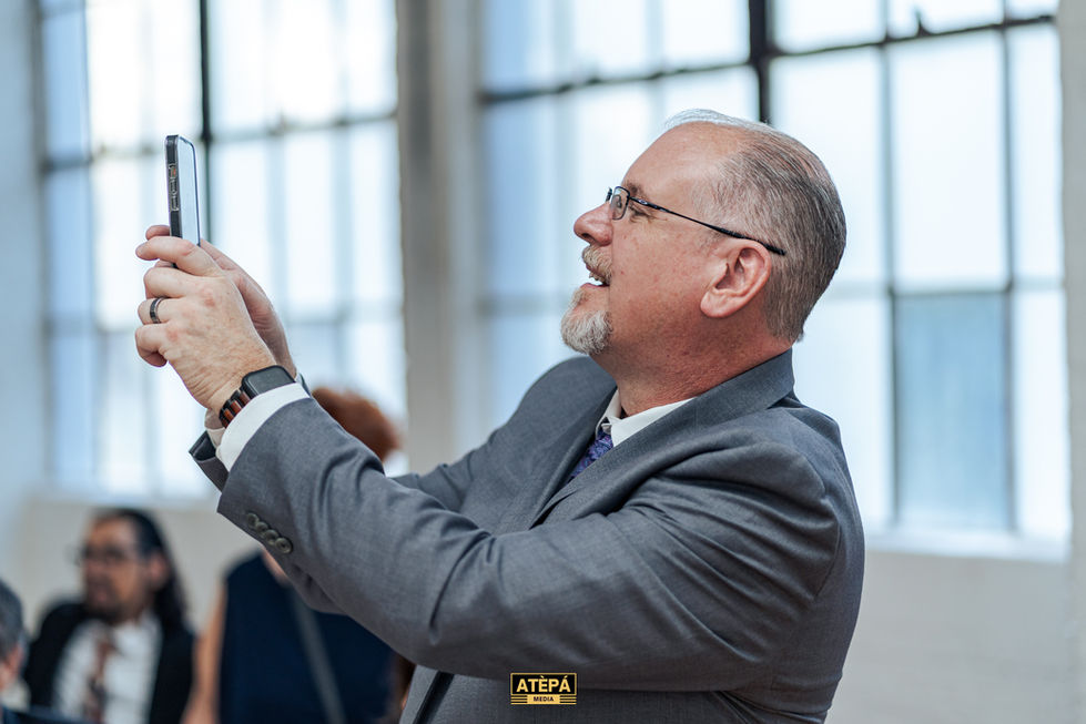 a man in a suit taking a picture with a tepe logo behind him