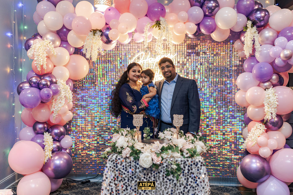 a man and woman holding a little girl in front of balloons and a sign that says happy birthday