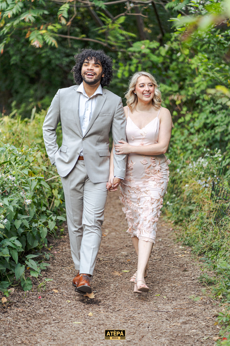 a man in a suit and a woman in a pink dress walk down a path