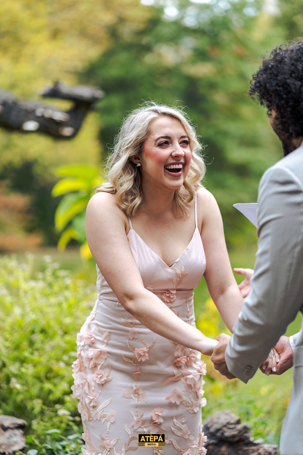 a woman in a pink dress laughs while holding hands with a man