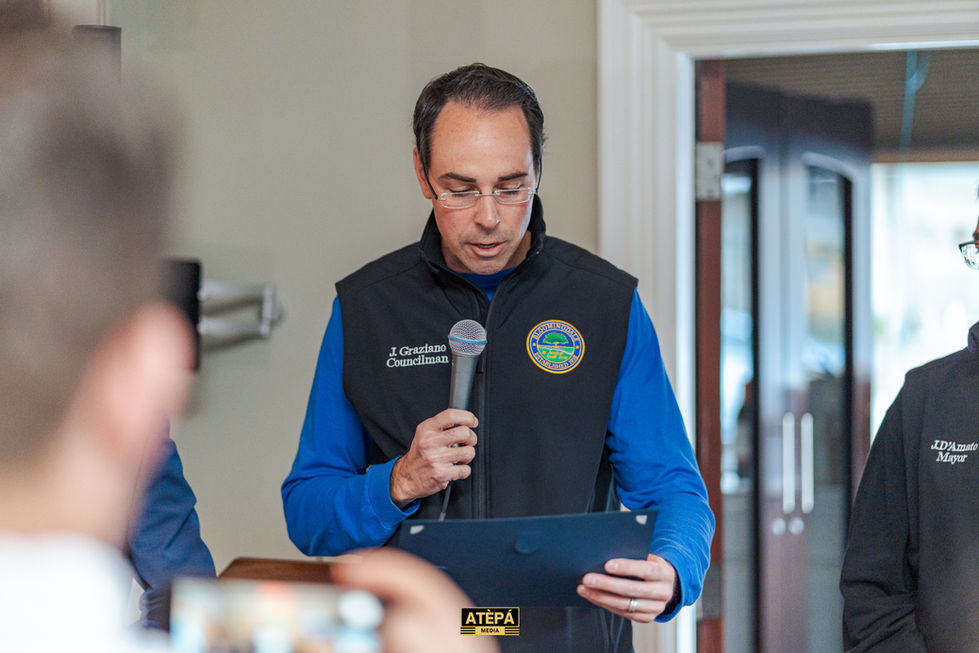 a man wearing a vest that says gordon councilman holds a microphone