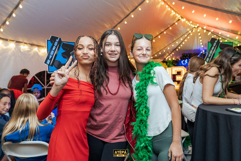 three girls posing for a picture with a sign in the background that says porsche