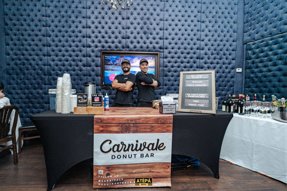 two men stand behind a carnivale donut bar
