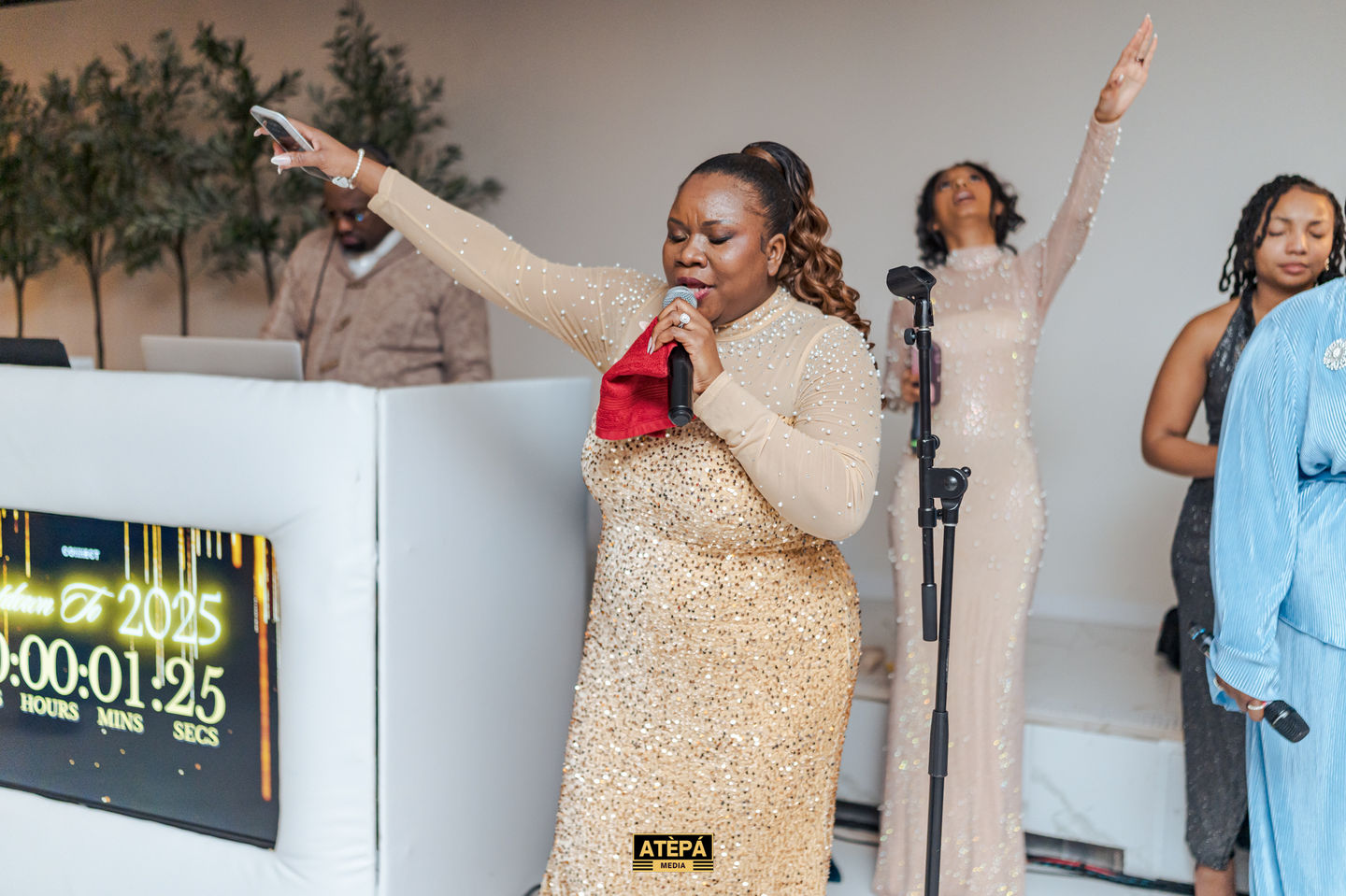 a woman in a gold sequined dress singing into a microphone with the word atepa on the bottom