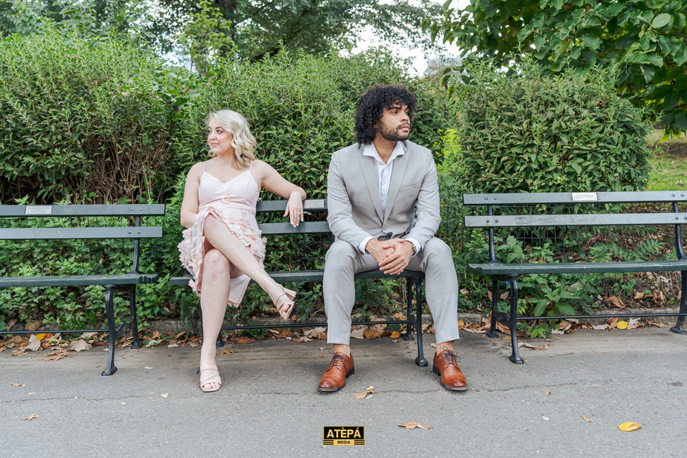 a man in a suit sits next to a woman in a pink dress on a park bench