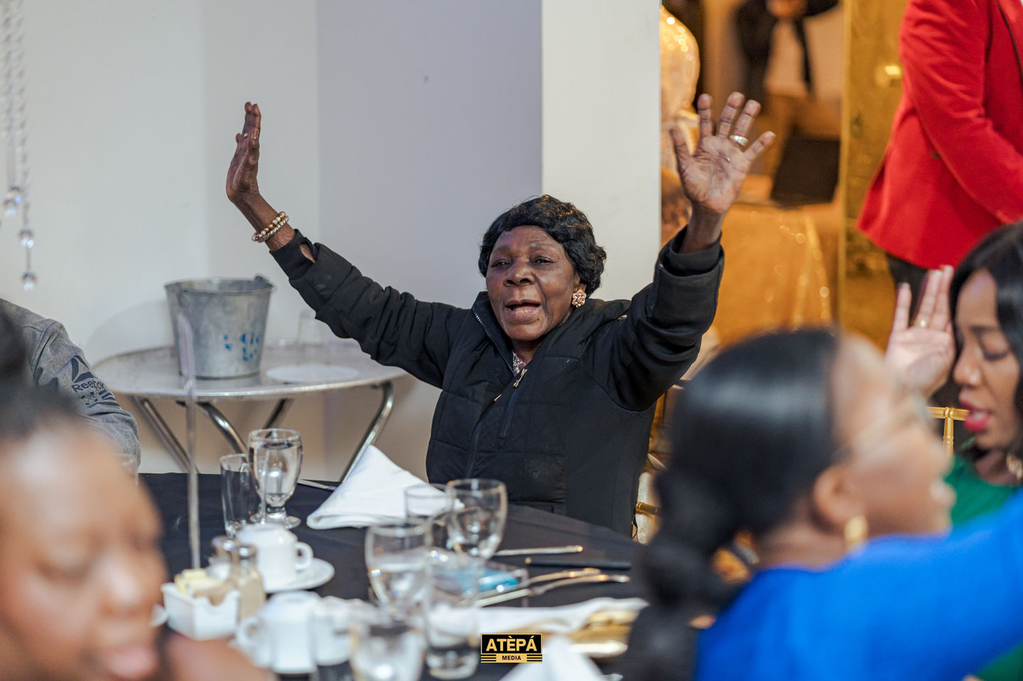 a woman sitting at a table with her hands in the air and a sign that says atepa