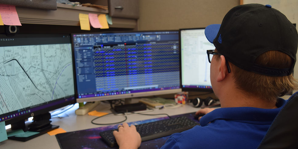 Professional reviewing complex geotechnical plans on a multi-monitor computer setup.