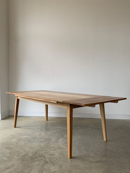 A traditional extending system dating back to the 15th century, the dutch pull out dining table with its self storing leaves provides a practical and simple solution for accommodating extra dinner guests. This piece is based on a design by Danish woodworker Tage Frid.
Ideal where space is a premium, the leaves are stored beneath the main table top, easily pulled out on wooden slides when needed.
Traditional breadboard ends frame the main table top, allowing seasonal wood movement but preventing warping. Below, a sturdy frame and splayed, tapered legs provide ample stability but with a delicate footprint.
Made to order from solid hardwood and finished in a durable matt hard wax oil to give a warm and natural appearance.