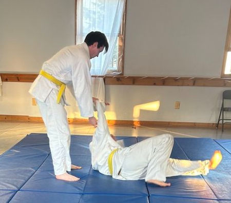Judo students practicing a throw on a blue mat.