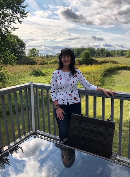 Susan standing outside on a wooden deck with meadow