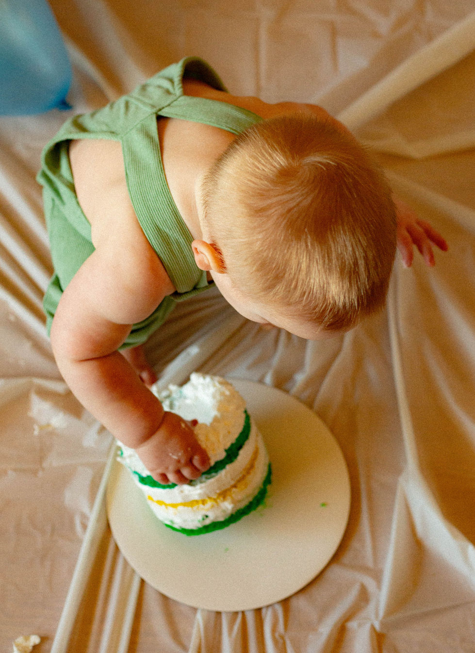 Overhead view of toddler leaning down to tip his cake over, edited in warm tones
