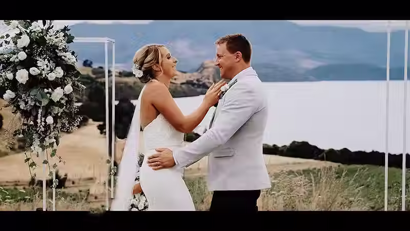 Wanaka wedding videography: Happy bride and groom laughing joyfully during their ceremony at The Rippon Hall, with Lake Wanaka in the background