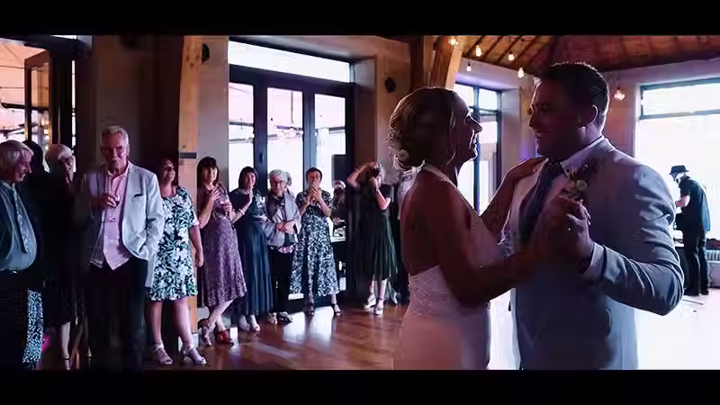 Wanaka wedding videography: Happy bride and groom sharing their first dance at The Rippon Hall reception, surrounded by smiling guests.