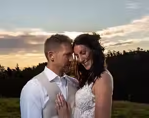 An intimate close-up portrait of a bride and groom embracing with closed eyes in a grassy field during a golden hour rustic farm wedding in Rangiora.