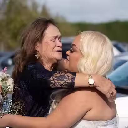 A touching candid shot of a mother crying and hugging her blonde bride next to a car, highlighting the emotional depth of Christchurch wedding photography by Kiwi Moments Media.