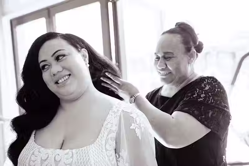 Bangor Farm wedding photography: bride smiling while someone adjusts her hair, black and white portrait. Christchurch wedding photographer Kiwi Moments Media.