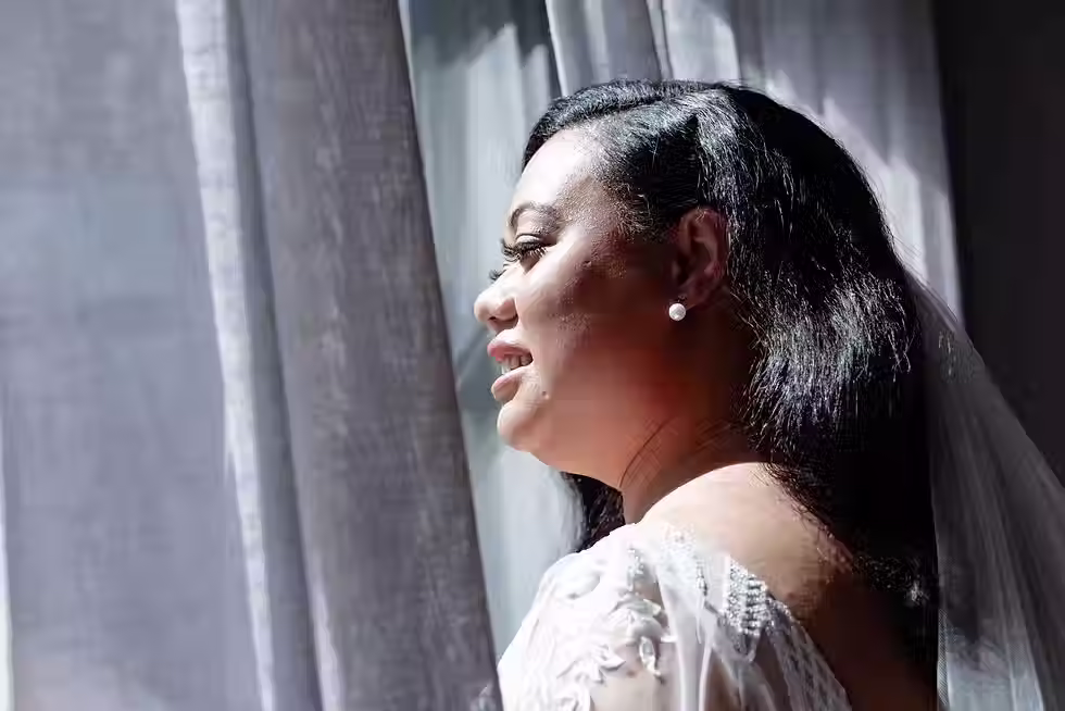 Bangor Farm wedding photography: bride in a white gown looking out a window with sunlight on her face, a beautiful portrait from Christchurch wedding photographer Kiwi Moments Media.