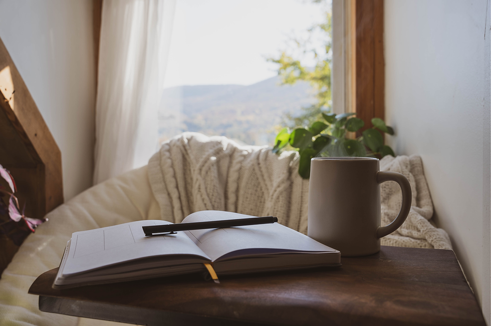 Ceramic mug and open book on a bed near a sunlit window, evoking the cozy and mindful tone of the brand.