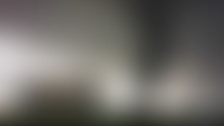 A large, dark tornado touches down near a small house in a rural landscape under a stormy, overcast sky.