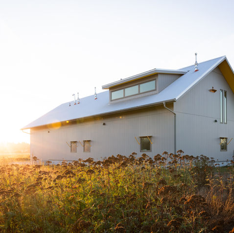 Vue en contre jour d'une grange moderne à la façade métallique entourée de champs au coucher de soleil