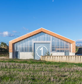 Photographie architecturale d'un hangar de stockage en structure bois et toit en pente au milieu d'un champ