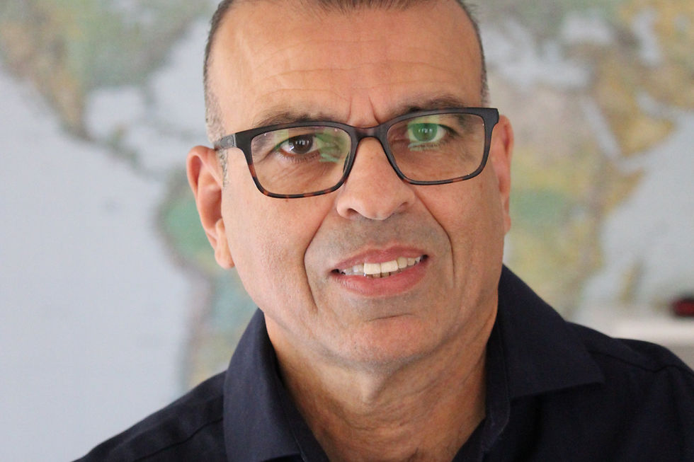 Portrait photo of Ali in a dark shirt, wearing glasses, with a blurred world map background