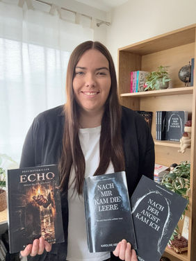 Karoline Aberger mit ihren veröffentlichten Büchern vor ihrem Bücherregal