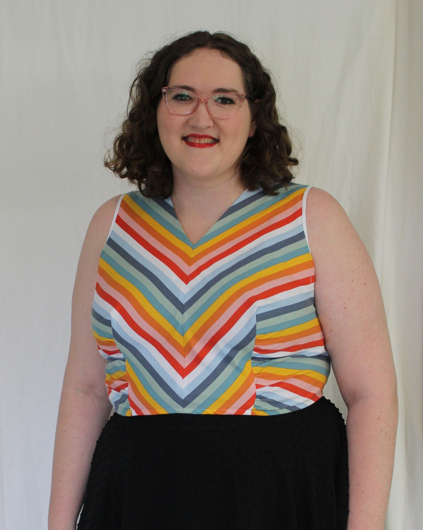 The front view of the Bevel Tank top. A woman is posing wearing the shirt to see the front. The tank has rainbow colored stripes.