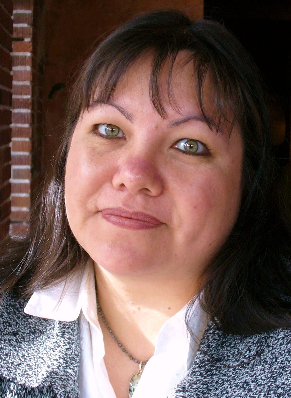 Photo of Tiffany Midge. She has brunette hair and green eyes, her head is titled to the left and is smiling warmly at the camera.