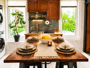 Kitchen table set for four beneath two windows with tree views in a furnished Greenpoint, Brooklyn apartment
