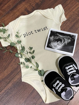 Pregnancy announcement image, featuring "plot twist" onesie and baby shoes