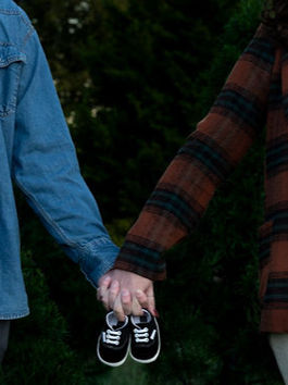 Pregnant couple holds hands with pair of baby shoes on their fingers