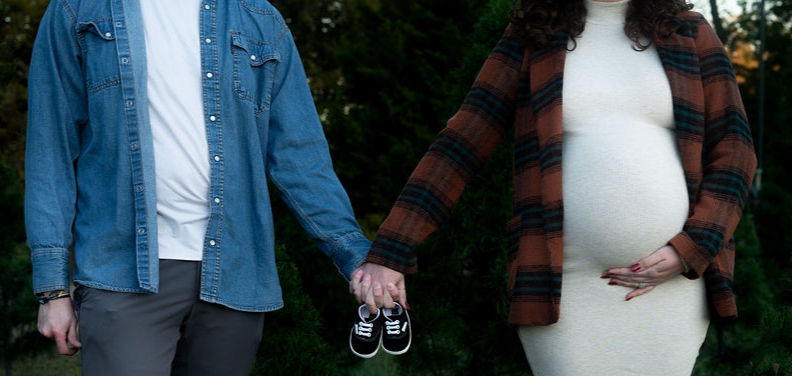 Pregnant couple holds hands with pair of baby shoes on their fingers