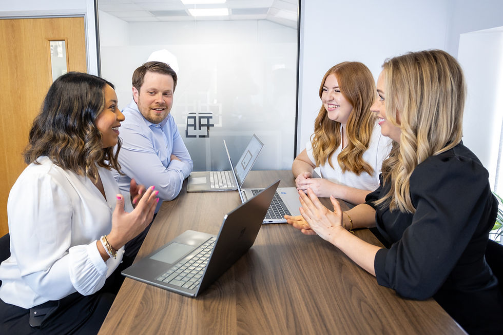4 smiling people sitting round an office table with their laptops