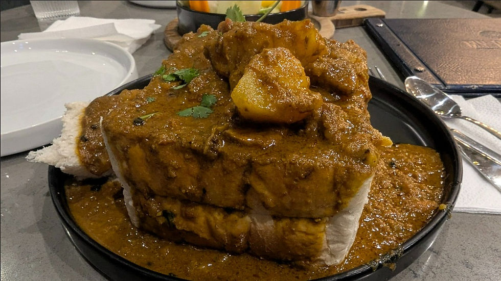 Bread bowl filled with spicy curry on a black plate. Garnished with cilantro. Background includes utensils and white napkins.